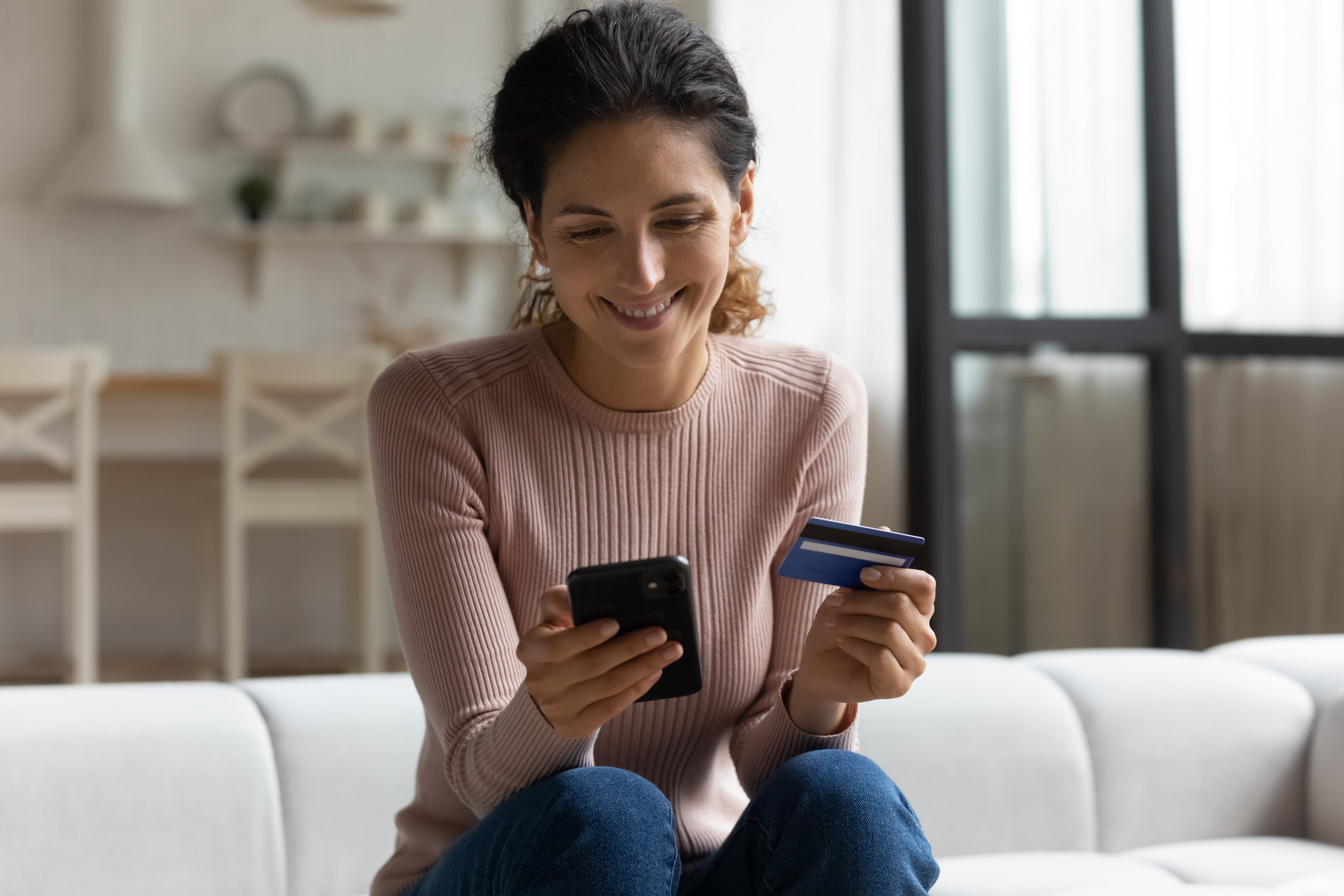 Smiling latina lady client holding mobile phone and credit card online shopping.