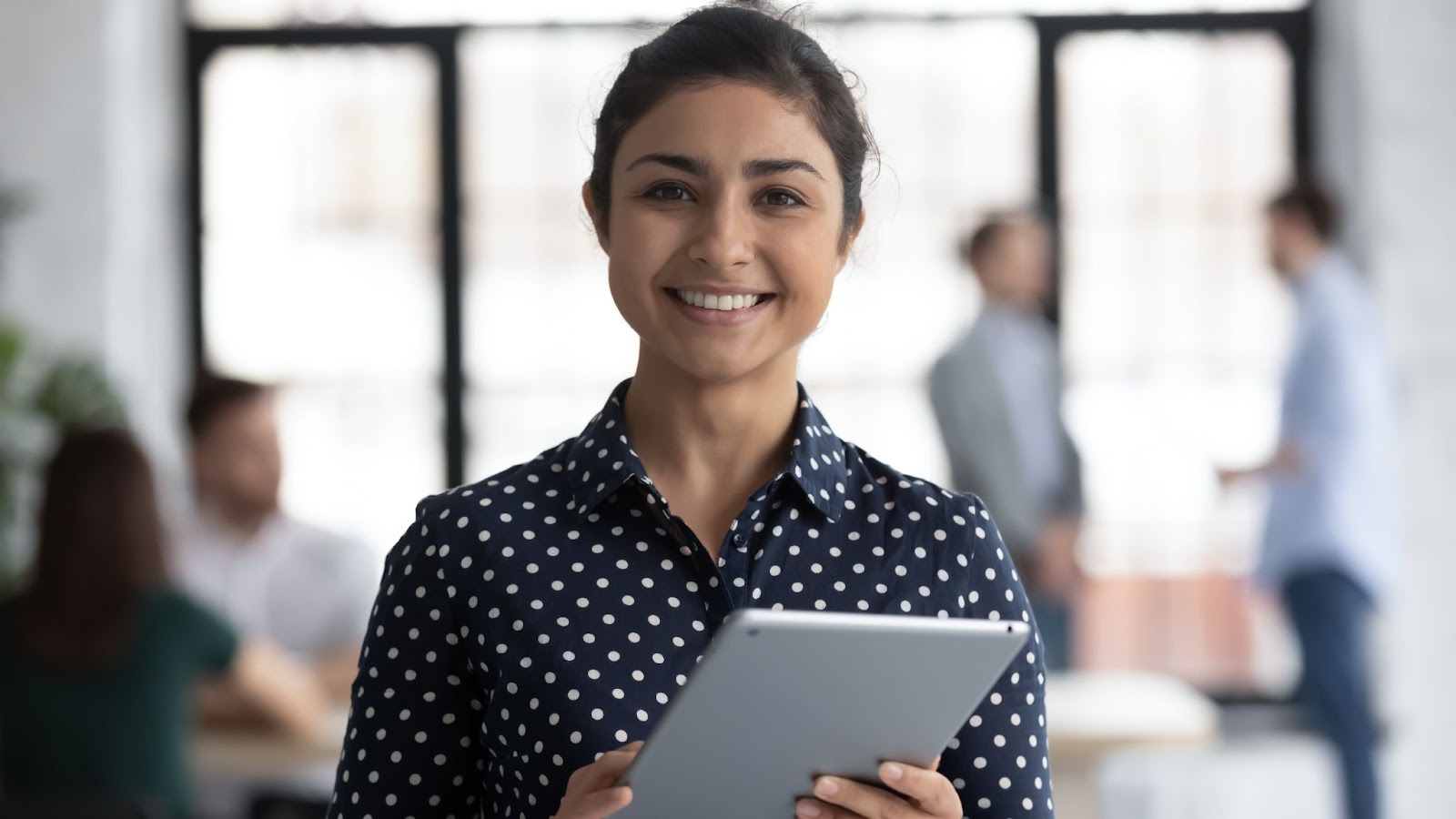 Portrait of a smiling female standing in an open space office holding a digital tablet