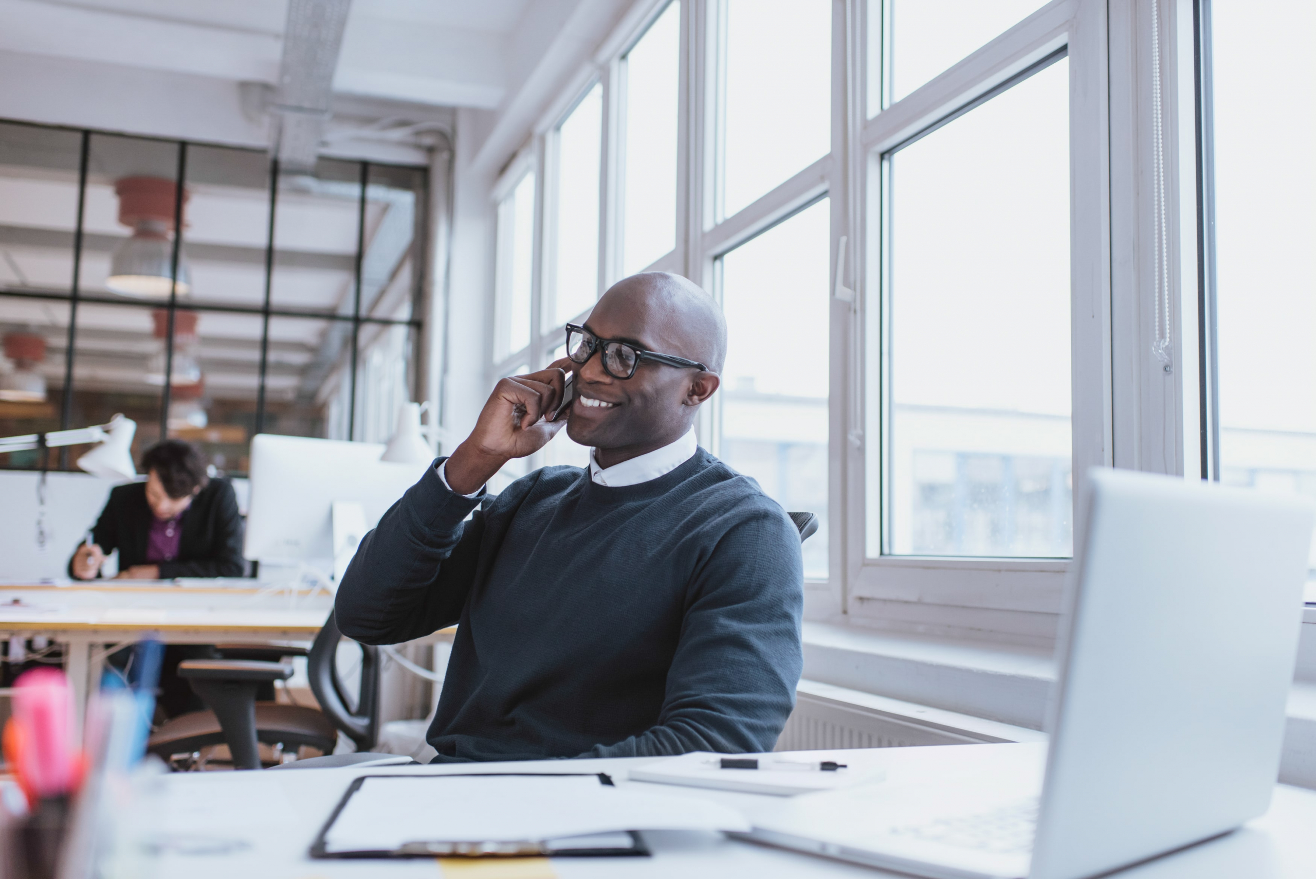 African American office worker at his desk smiling while talking on his cell phone