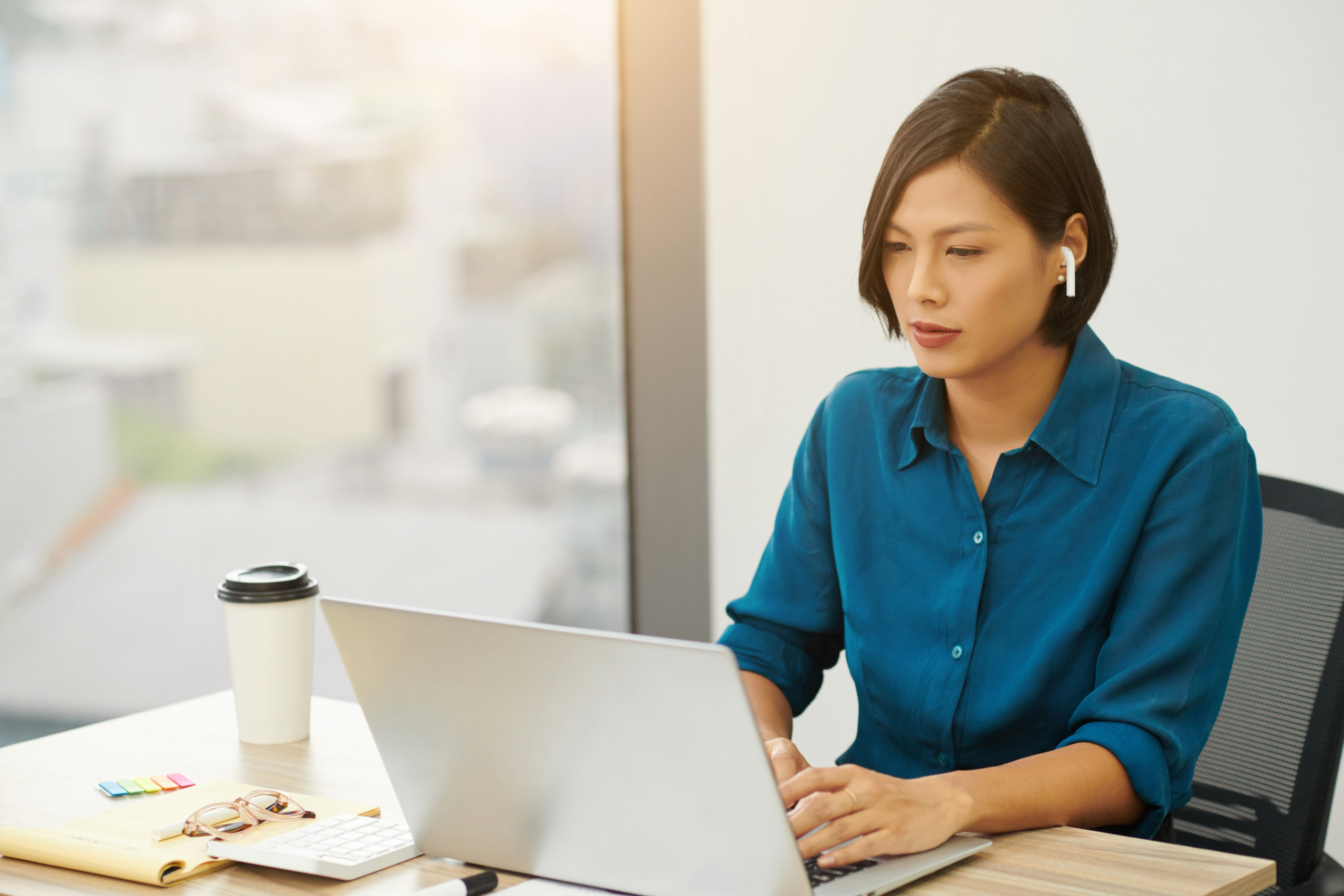 Asian female salesperson with earphones in looking at her computer