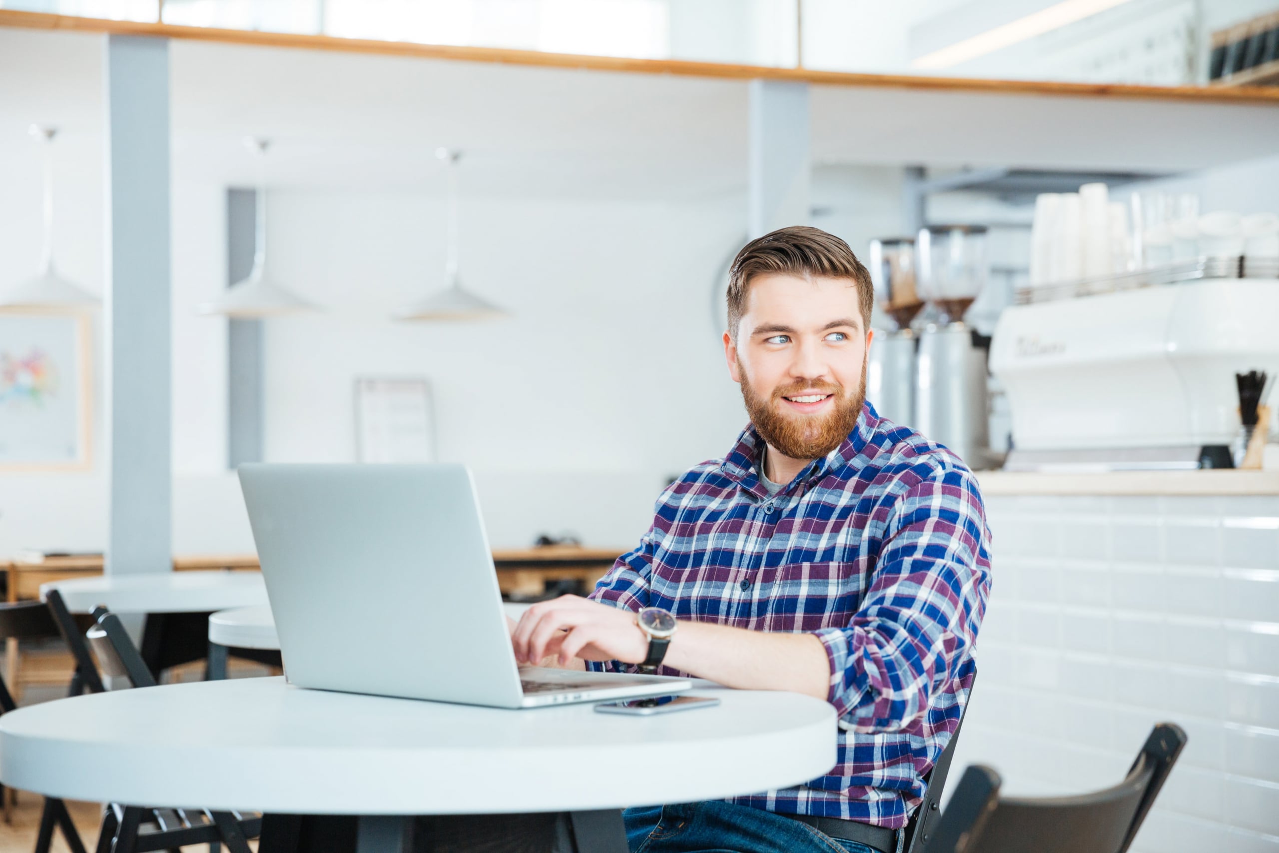 Young bearded man sitting at a table smiling while typing on his laptop